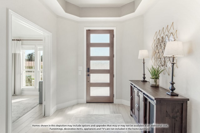 foyer entrance with light hardwood / wood-style floors and a tray ceiling