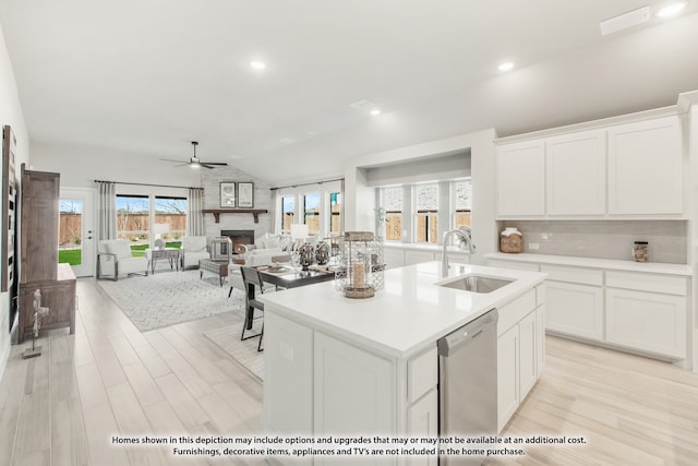 kitchen with a large fireplace, sink, a center island with sink, dishwasher, and white cabinetry