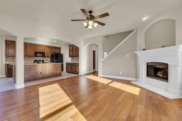 unfurnished living room featuring a fireplace, light wood-type flooring, ceiling fan, and sink