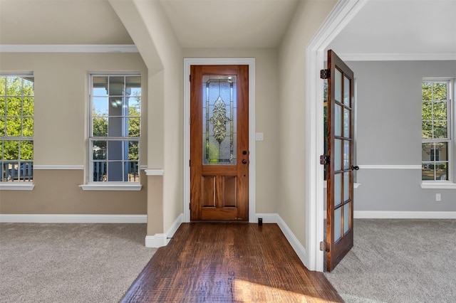 foyer featuring dark carpet, crown molding, and a wealth of natural light