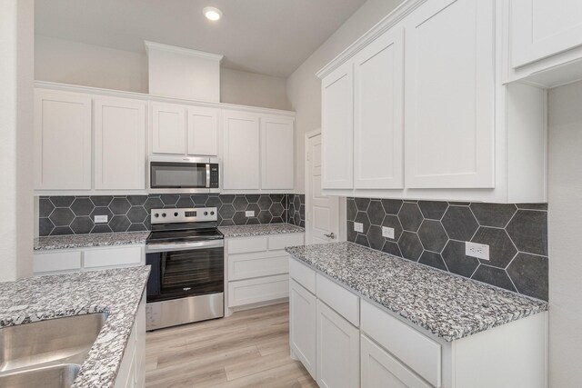 kitchen with light stone countertops, stainless steel appliances, light hardwood / wood-style flooring, decorative backsplash, and white cabinets