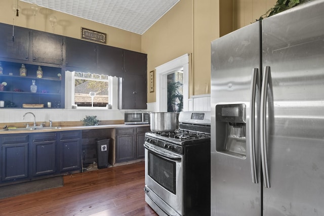 kitchen with blue cabinets, a sink, light countertops, appliances with stainless steel finishes, and dark wood finished floors