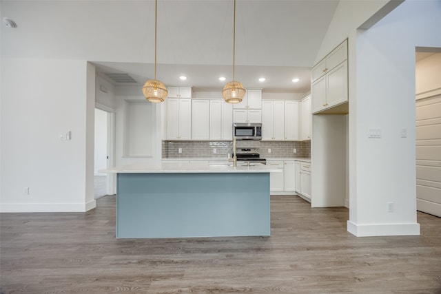 kitchen featuring stainless steel appliances, decorative light fixtures, a kitchen island with sink, white cabinets, and light wood-type flooring