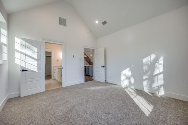 unfurnished bedroom with high vaulted ceiling, light colored carpet, and connected bathroom