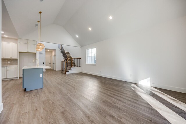 unfurnished living room featuring sink, high vaulted ceiling, and light hardwood / wood-style floors