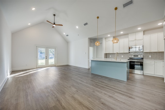 kitchen with appliances with stainless steel finishes, light wood-type flooring, pendant lighting, high vaulted ceiling, and white cabinetry