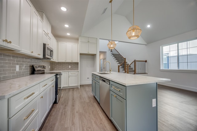 kitchen featuring appliances with stainless steel finishes, sink, decorative light fixtures, a center island with sink, and light hardwood / wood-style floors