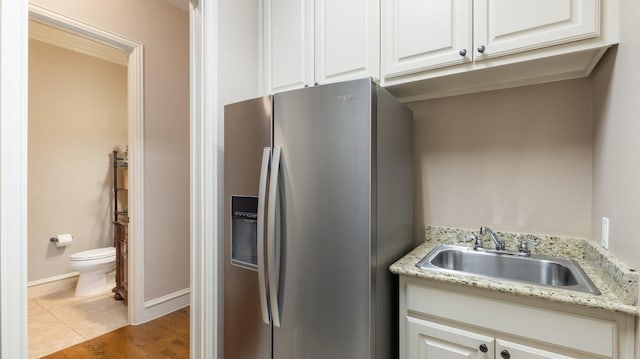 kitchen featuring light stone countertops, stainless steel fridge, light wood-type flooring, sink, and white cabinets