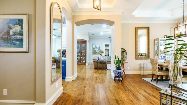 corridor with a raised ceiling, crown molding, and wood-type flooring