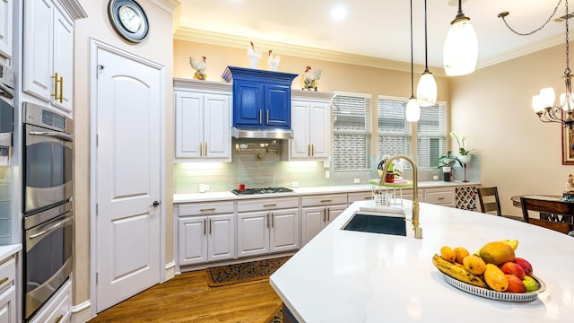 kitchen featuring hardwood / wood-style floors, pendant lighting, sink, ornamental molding, and stainless steel appliances