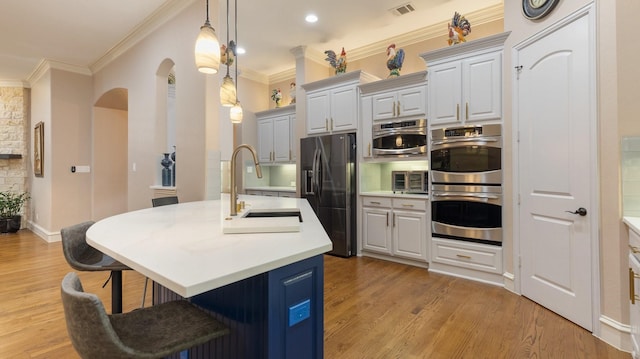 kitchen featuring appliances with stainless steel finishes, crown molding, light hardwood / wood-style floors, a breakfast bar area, and an island with sink