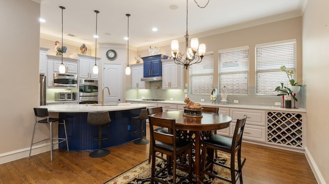 kitchen featuring a kitchen island with sink, dark hardwood / wood-style floors, ornamental molding, appliances with stainless steel finishes, and a breakfast bar area