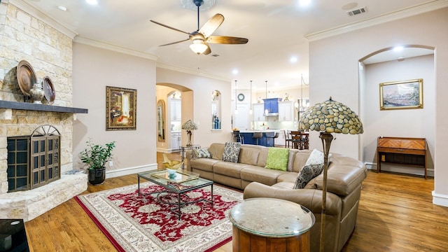 living room featuring hardwood / wood-style flooring, ceiling fan, ornamental molding, and a fireplace