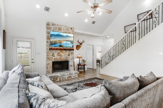 living room with ceiling fan, light hardwood / wood-style floors, a stone fireplace, and high vaulted ceiling