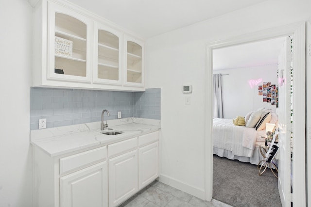 kitchen featuring sink, tasteful backsplash, light stone counters, light carpet, and white cabinets