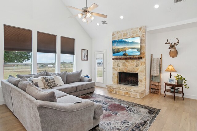 living room with light wood-type flooring, high vaulted ceiling, ceiling fan, and a stone fireplace