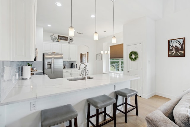 kitchen with kitchen peninsula, stainless steel refrigerator with ice dispenser, light wood-type flooring, sink, and white cabinets