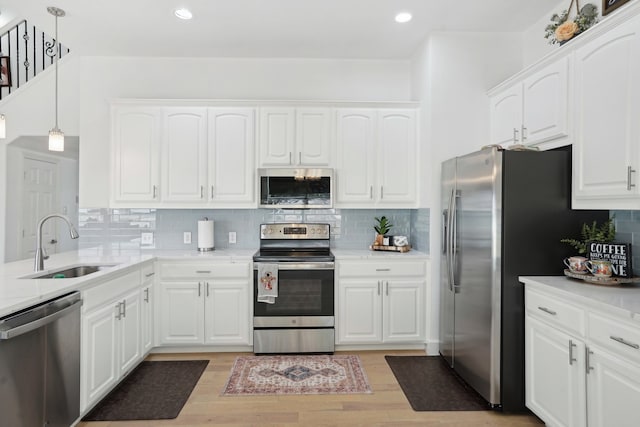 kitchen with appliances with stainless steel finishes, light wood-type flooring, sink, pendant lighting, and white cabinetry