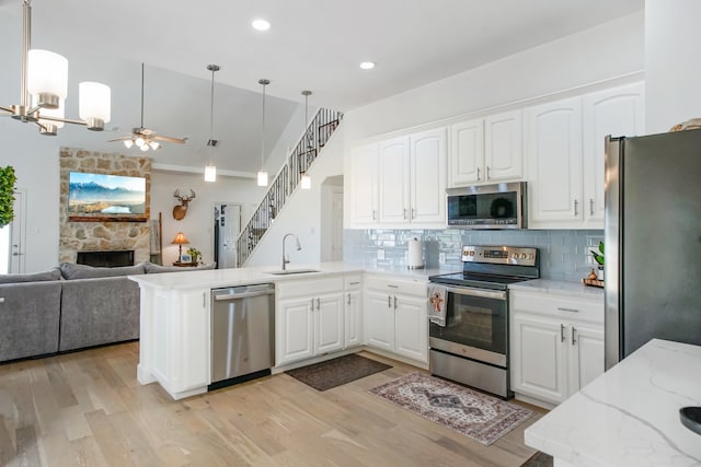 kitchen with white cabinets, light hardwood / wood-style flooring, appliances with stainless steel finishes, decorative light fixtures, and kitchen peninsula