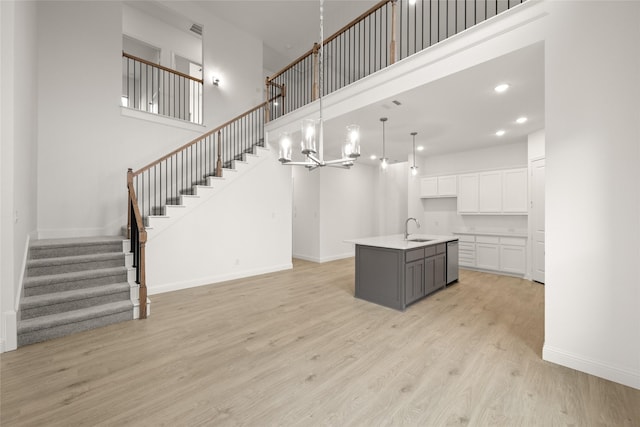 kitchen featuring baseboards, an island with sink, a sink, light wood-style floors, and white cabinetry