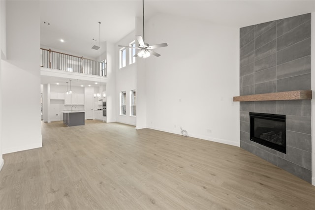 unfurnished living room with light wood finished floors, baseboards, ceiling fan, a tile fireplace, and a sink