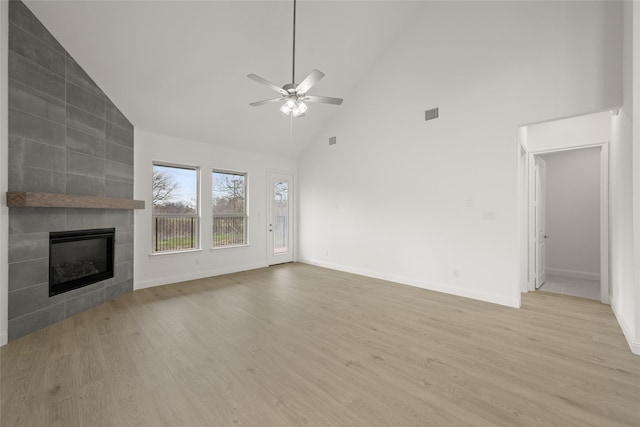 unfurnished living room with a tiled fireplace, light wood-style floors, baseboards, and ceiling fan