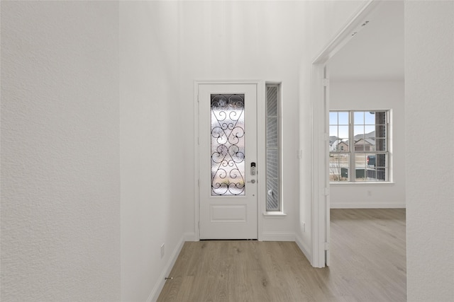 foyer featuring light wood-style floors, baseboards, and a textured wall