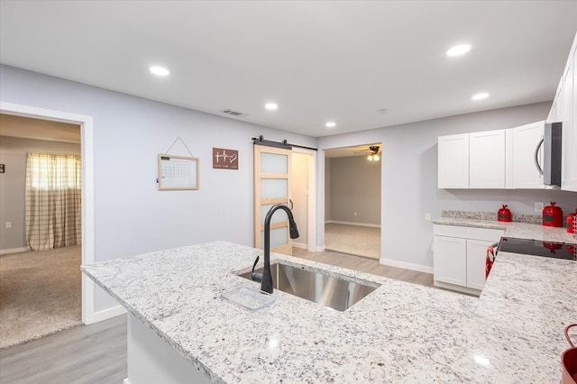 kitchen with light stone countertops, a barn door, white cabinetry, and sink