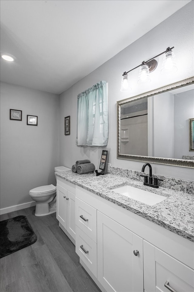 bathroom with hardwood / wood-style floors, vanity, toilet, and walk in shower