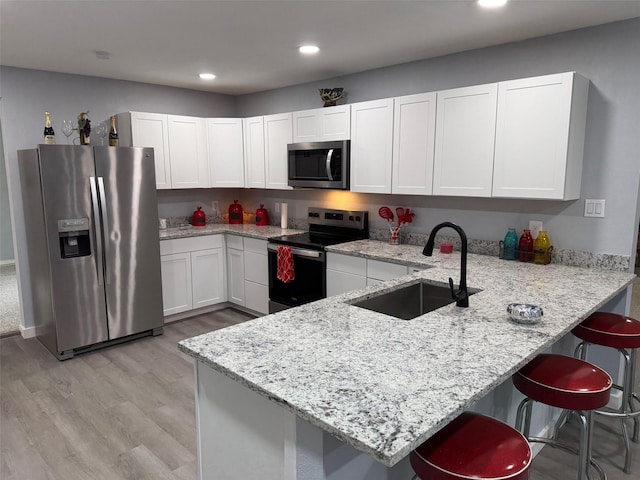 kitchen with appliances with stainless steel finishes, a peninsula, light stone countertops, white cabinetry, and a sink