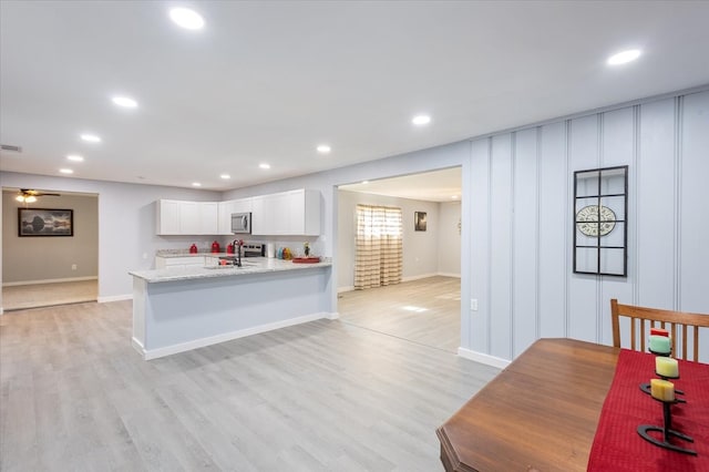 kitchen with white cabinets, sink, light hardwood / wood-style flooring, light stone counters, and kitchen peninsula