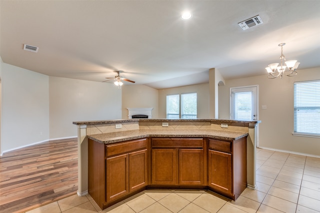 kitchen with pendant lighting, a center island, ceiling fan with notable chandelier, light wood-type flooring, and light stone counters