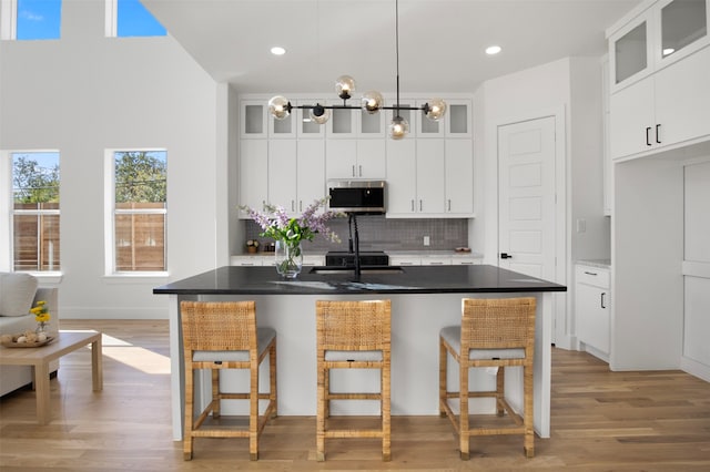 kitchen with white cabinetry, a kitchen bar, decorative backsplash, a center island with sink, and light wood-type flooring