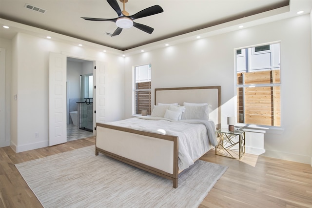 bedroom with multiple windows, a raised ceiling, connected bathroom, and light hardwood / wood-style flooring