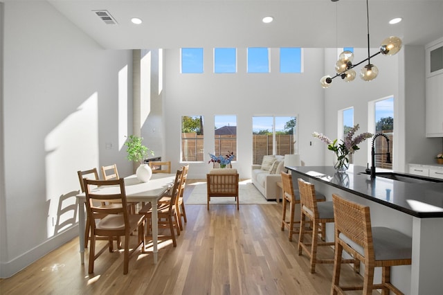 dining space featuring a high ceiling, sink, a notable chandelier, and light hardwood / wood-style floors