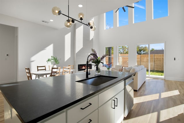 kitchen with sink, a fireplace, light hardwood / wood-style floors, white cabinets, and a center island with sink