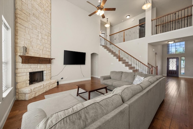 living room featuring hardwood / wood-style flooring, stairway, a ceiling fan, a stone fireplace, and baseboards