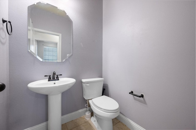 half bath featuring baseboards, toilet, tile patterned floors, and a sink