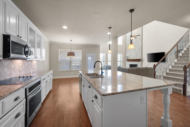 kitchen with wood finished floors, a stone fireplace, tasteful backsplash, appliances with stainless steel finishes, and a sink