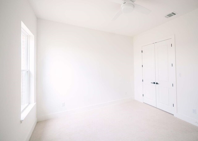 unfurnished bedroom featuring multiple windows, ceiling fan, a closet, and light colored carpet