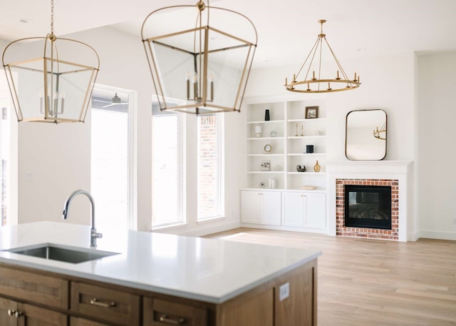 kitchen with pendant lighting, a kitchen island with sink, sink, a brick fireplace, and light hardwood / wood-style floors