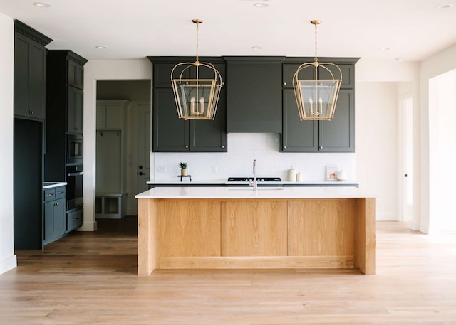 kitchen featuring light wood-type flooring, a center island with sink, black oven, and a notable chandelier