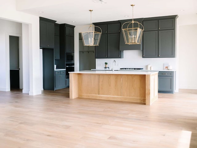 kitchen with light wood-type flooring, a kitchen island with sink, decorative light fixtures, black oven, and stainless steel microwave