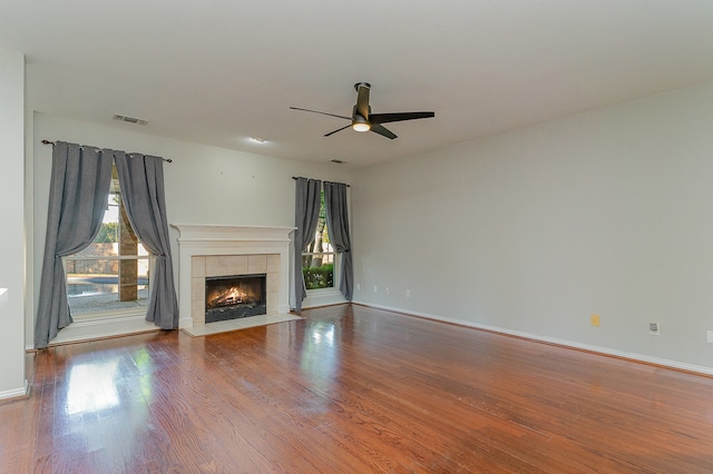 unfurnished living room with a tile fireplace, wood-type flooring, and ceiling fan