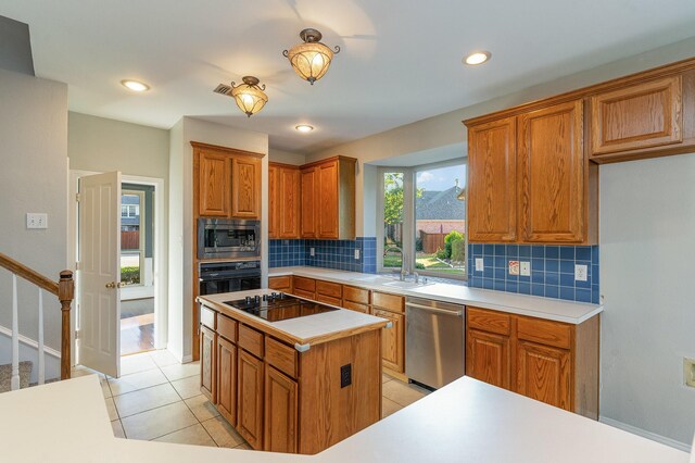 kitchen with sink, light tile patterned floors, decorative backsplash, a kitchen island, and black appliances