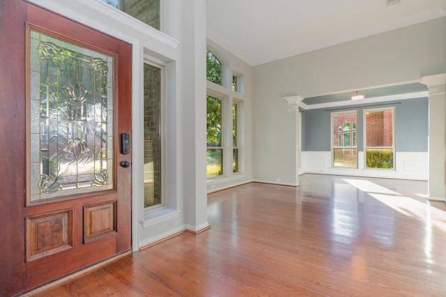 foyer with decorative columns, a wealth of natural light, ornamental molding, and hardwood / wood-style flooring