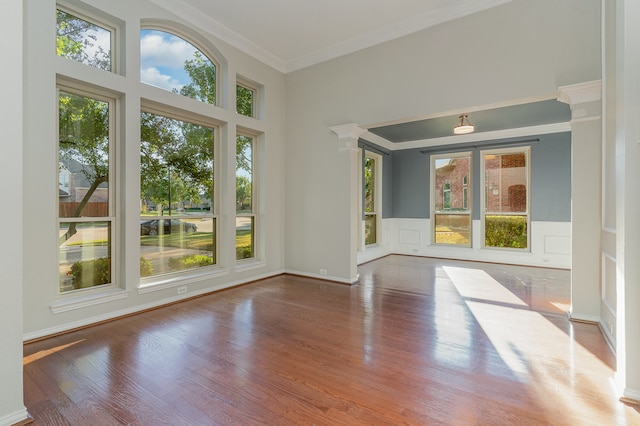 unfurnished room featuring hardwood / wood-style floors, ornate columns, ornamental molding, and a wealth of natural light