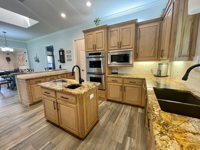 kitchen with light wood-type flooring, stainless steel appliances, a kitchen island with sink, and sink