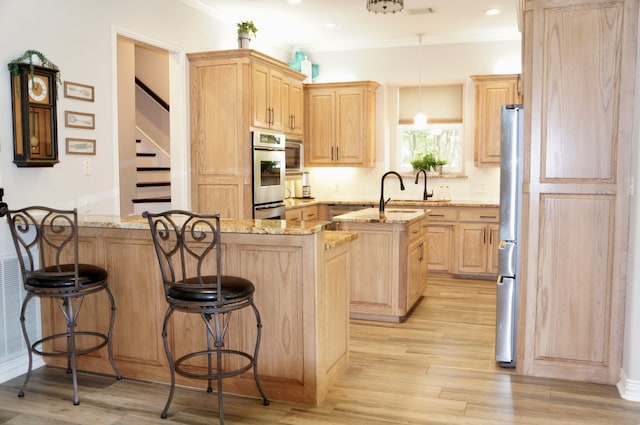 kitchen featuring light stone countertops, a kitchen breakfast bar, light wood-type flooring, light brown cabinets, and a center island with sink