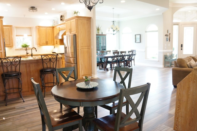 dining area featuring ornamental molding, a healthy amount of sunlight, light wood-type flooring, and a notable chandelier